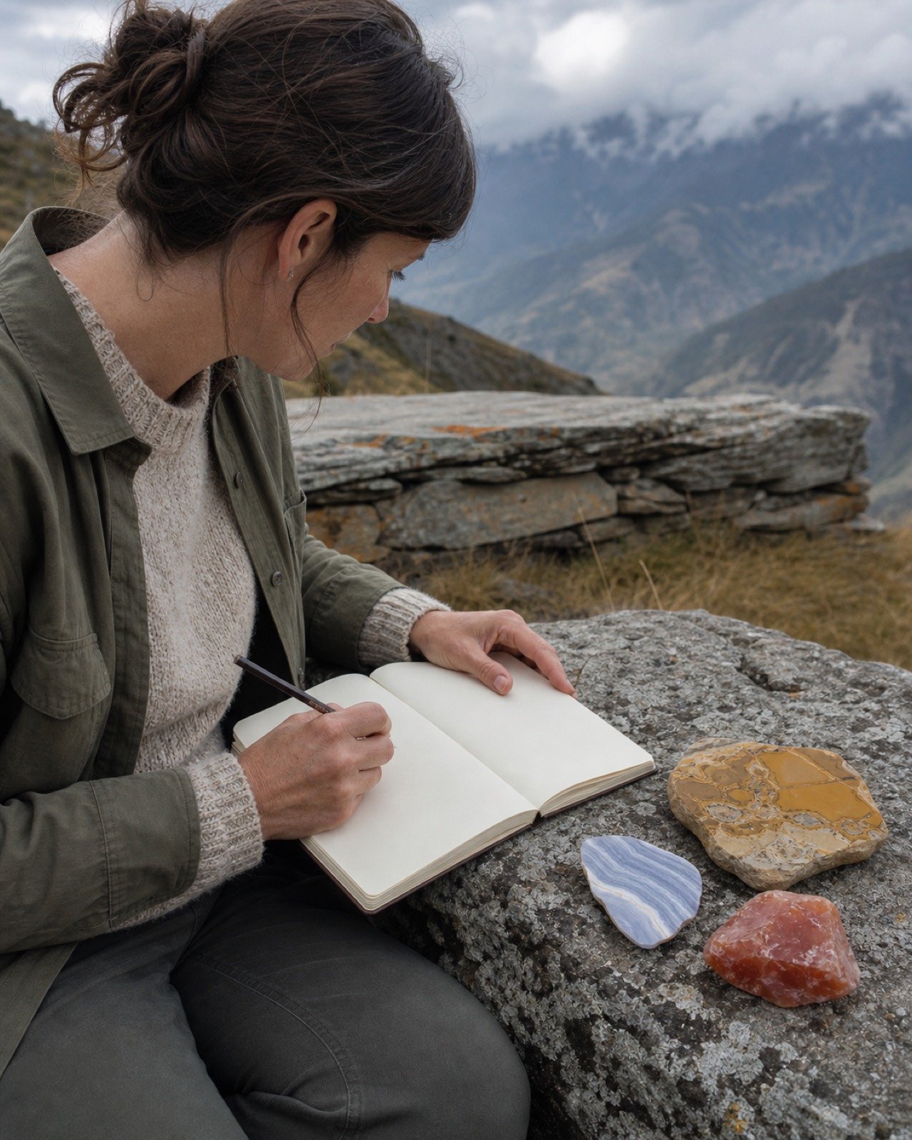 Chalcedony ritual: a woman writing in a field notebook beside agate, jasper, and carnelian in a Himalayan landscape