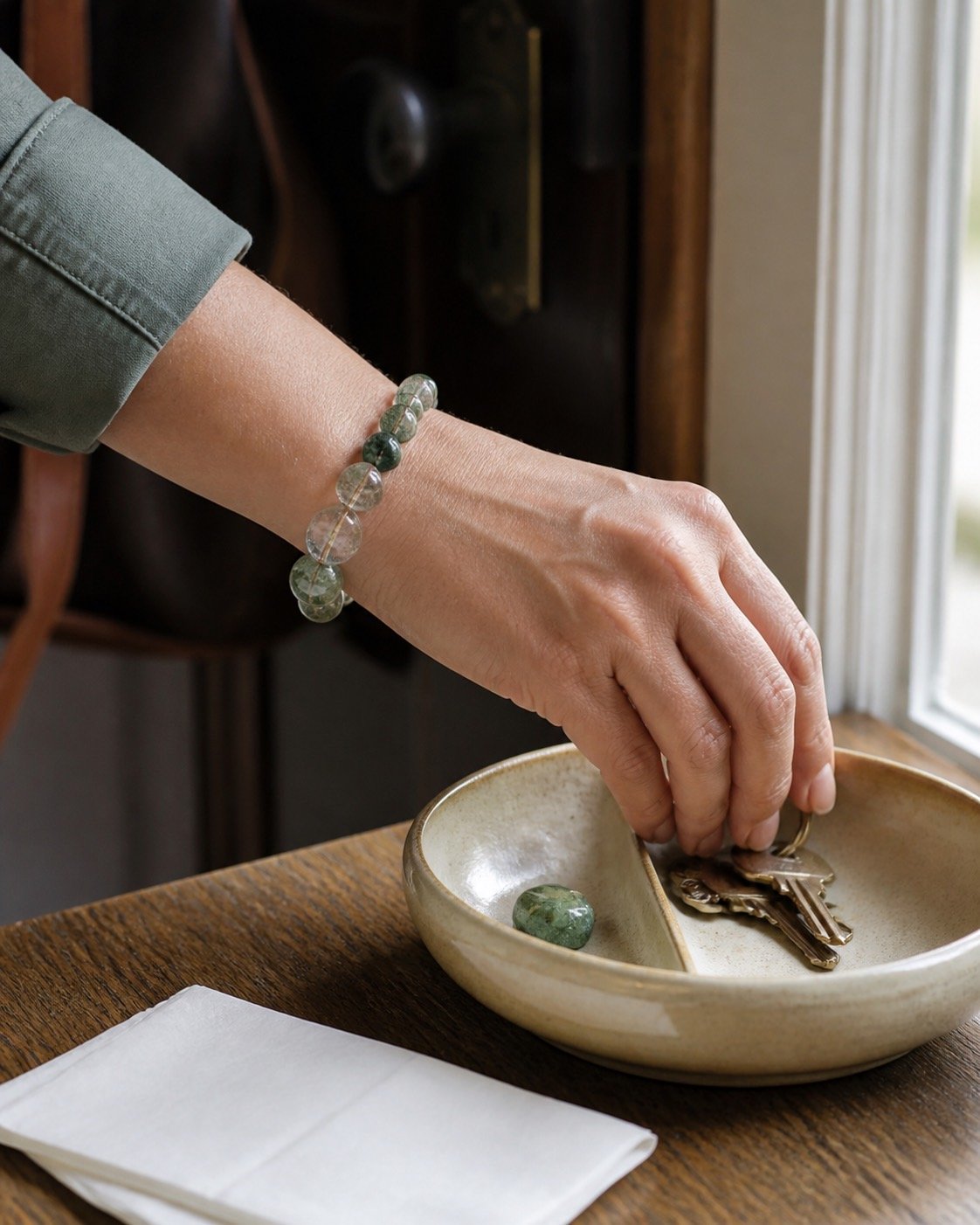 A hand places keys into a shallow entryway bowl beside a green stone