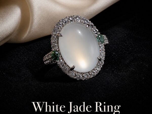 White Jade Clarity Ring with an oval white cabochon, halo of clear stones and small green side accents on a dark display surface.