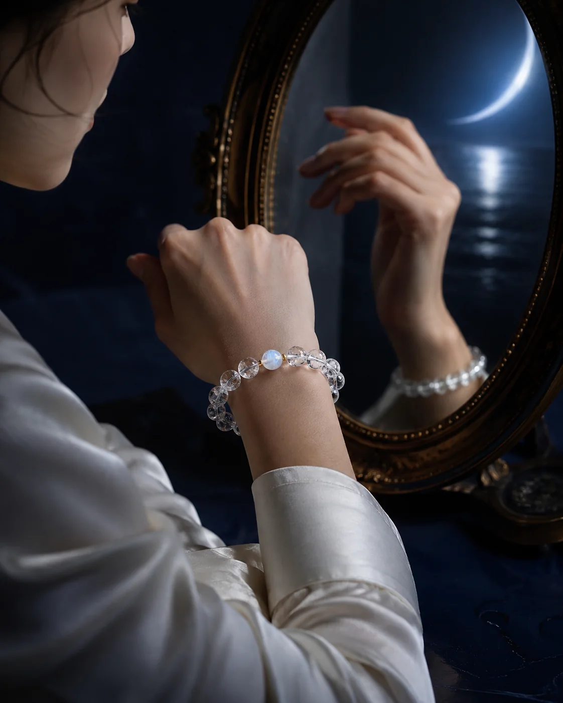 Model wearing a clear quartz and moonstone bracelet beside an antique mirror in moonlight