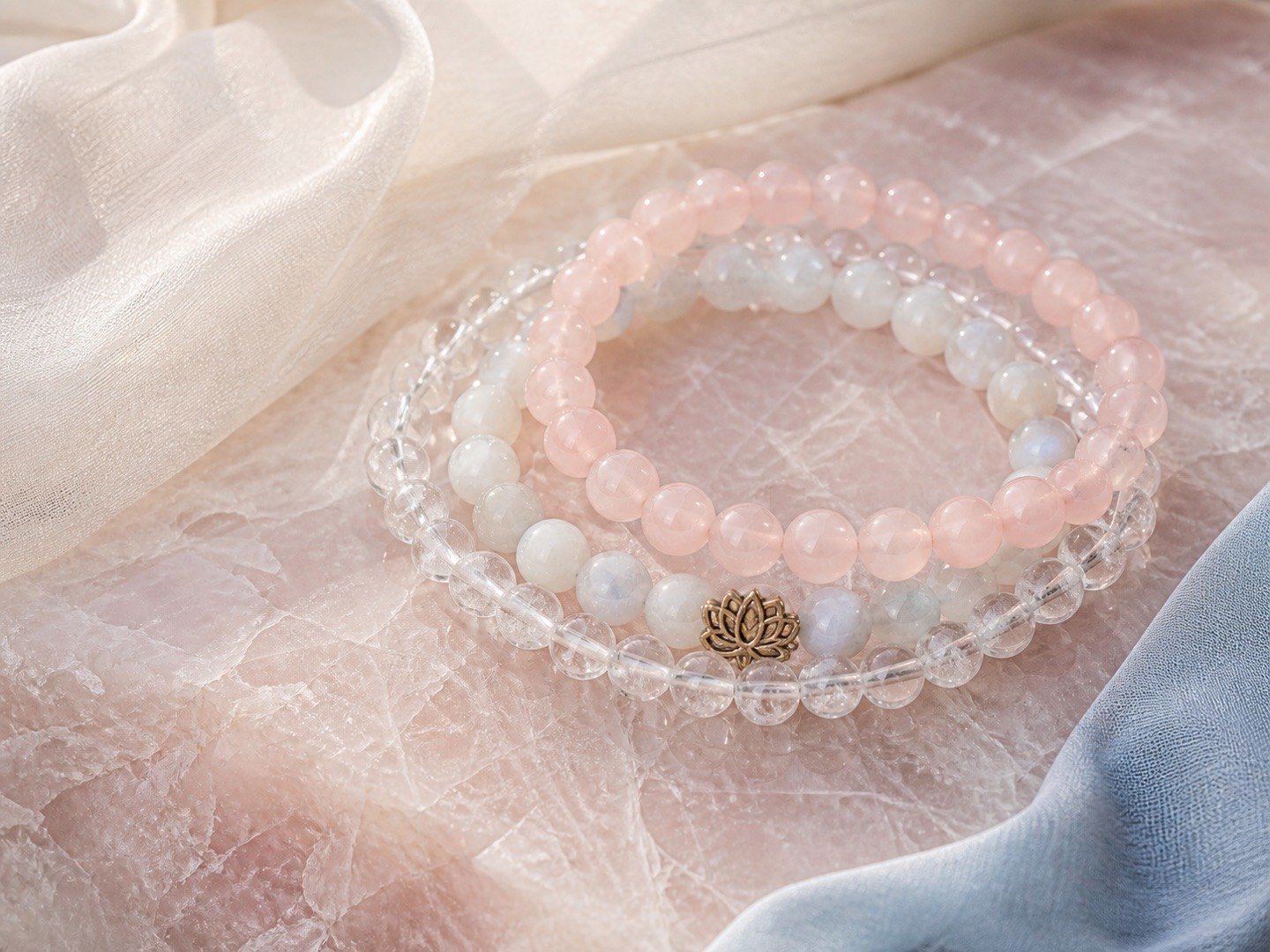 Rose quartz, moonstone, and clear quartz bracelets layered on blush stone